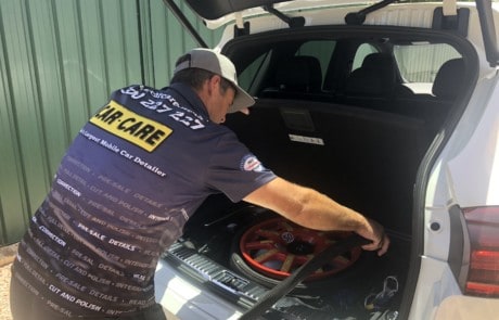 A car detailer performing an interior detail clean on the boot of a car using a vaccum cleaner to clean by the spare wheel